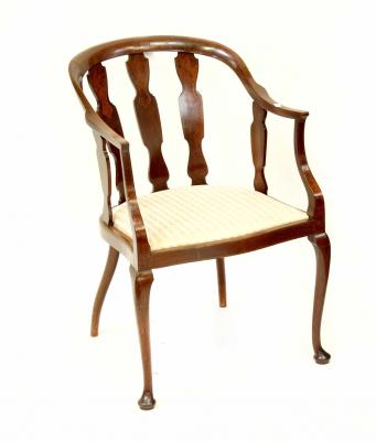 An Edwardian mahogany elbow chair with curved back and arms, supported by shaped spindles over shaped seat with fabric upholstery, raised on cabriole front legs.