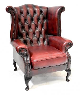 A modern button back wing armchair upholstered in oxblood studded leather, on cabriole legs.