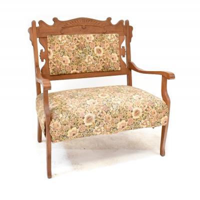 An Edwardian oak-framed settee of small proportions with carved back rest and upholstered in a woven floral fabric, length 87cm.