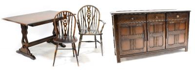 A priory-style oak dining suite comprising a table, 76 x 140 x 82cm, six wheel back dining chairs (5+1) and a sideboard with three drawers and three fielded and panelled cupboard doors, on stile feet, 87 x 154 x 47cm.