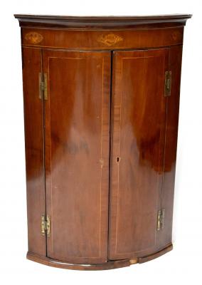 A George III mahogany bow-front wall-hanging corner cupboard, inlaid with shell motifs, with a pair of crossbanded and strung doors, shelved interior, 106 x 76 x 50cm.