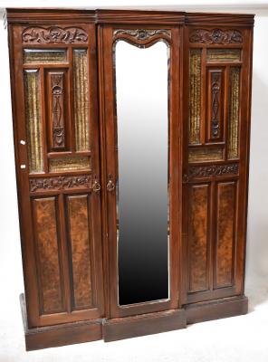A Victorian walnut triple break-front wardrobe, the central door with bevelled mirror plate flanked by pair of part glazed doors set with carved motifs and fielded panels, raised on plinth base, 200 x 150 x 53cm.