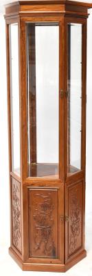 A contemporary Oriental hardwood hexagonal display cabinet, the upper section with bevelled glass, a pair of doors with three adjustable shelves to the interior above grape and vine carved panels, raised on a plinth base, 198.5 x 67cm.