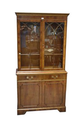 A reproduction yew wood bookcase with dentil moulded cornice above pair of glazed doors enclosing two adjustable shelves, above base section with pair of drawers above pair of panelled doors, raised on bracket feet, 194 x 99 x 37cm.