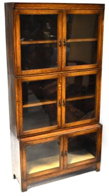 A 1930s oak three-tier bookcase, each tier with a pair of glazed cupboard doors, with metal peardrop handles, the lower tier deeper than the upper two and on bracket feet, 168.5 x 88 x 28.5cm.
