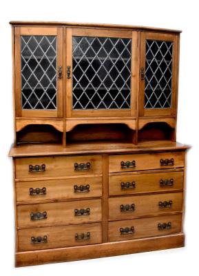 An early 20th century stained pine dresser, the top with three leaded glazed doors above a base of eight drawers, all with Arts & Crafts style drop handles, on a plinth base, 195 x 152 x 46cm.
