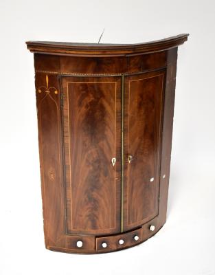 A 19th century flame mahogany inlaid wall-hanging corner cabinet, stepped and inlaid frieze above twin bow front cupboard doors, with ivory escutcheon, above three small drawers, each with later porcelain knobs, 107 x 79 x 55cm.