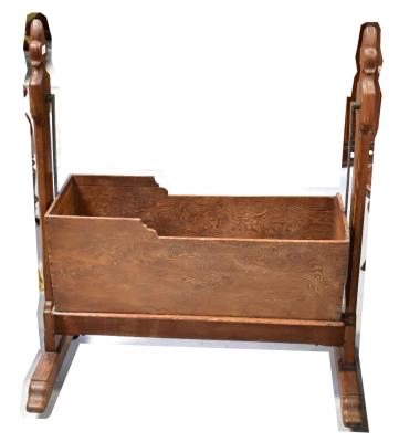 A 19th century pine swinging crib with Gothic inspired side supports and base united with cross-stretcher, raised on metal castors, height 110cm, width 92cm.
