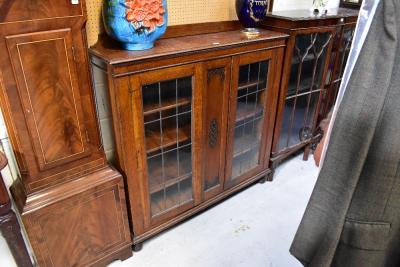 An early 20th century oak two-door display cabinet, with central blind fret carved panel flanked by pair of leaded glazed doors, raised on bun feet, 123.5 x 122 x 30cm.