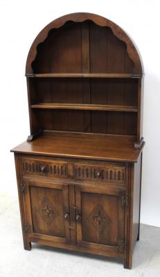 An early 20th century oak Jaycee Priory-style Welsh dresser of small proportions, arched back with two plate racks over two frieze drawers, two cupboard doors, with floral carving to bracket supports, 170 x 93cm.