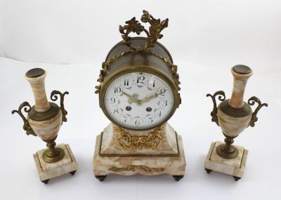 An early 20th century French drum clock on marble base with garniture, the dial set with Arabic numerals and decorated with swags and floral festoons, encasing a twin-train movement striking on bell, the garniture as two in the same pink marble, height of clock 37.5cm (3).