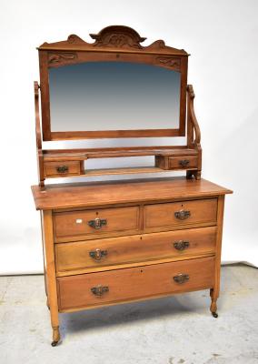 An early 20th century walnut dressing chest, the arched bevelled mirror plate within carved frame, above open shelf with short drawer either side, above a base of two short and two long drawers, raised on turned supports to castors, 171 x 107 x 46cm.