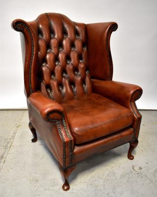 A reproduction dark tan leather button pressed and stud decorated wingback armchair, raised on cabriole supports to pad feet.