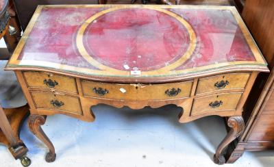 A reproduction walnut Georgian-style serpentine fronted lowboy, the top set with three gilt tooled oxblood leather panels, above central frieze drawer flanked by a pair of drawers to either side and a shaped apron, raised on carved cabriole supports to scrolling feet, 79 x 108 x 56cm (af).