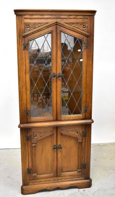 A reproduction oak glazed corner cupboard, the top with pair of leaded doors, within carved borders, on a cupboard base with fielded and panelled doors, on bracket feet, 181 x 77 x 38cm.
