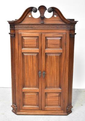 A mahogany wall-hanging flat-fronted corner cupboard, the broken swan neck pediment centred with a carved shell motif, above blind fret carved frieze and pair of fielded panelled doors flanked by reeded pilasters, enclosing two shaped shelves above small panelled door, flanked by a pair of drawers, with further internal reeded pilasters and blind fret carved detail, 142 x 91 x approx 48cm. Footnote: From the estate of local architect Herbert Rowse, famous for the design of Martins Bank, the Phil