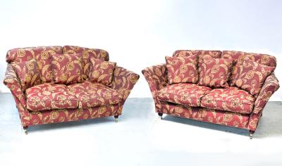 A pair of contemporary three-seat sofas upholstered in maroon fabric, with gold floral sprays, outswept arms, raised on turned supports to brass caps and castors (2).