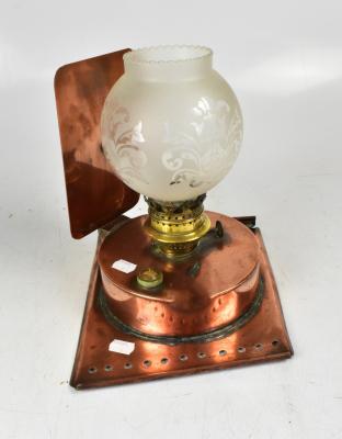 A copper oil lamp on rectangular stand and reflective back plate, height 28cm.