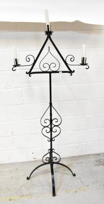 A wrought iron free standing three-branch candelabrum with triangular upper section centred with scrolling motif, further surmounted with scrolling outswept branches above a wrythen twist column, with scrolling details and quadripartite base, height 159cm.