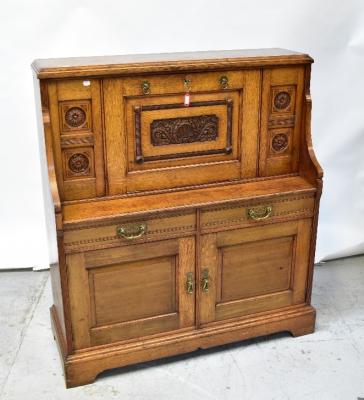 A Victorian oak bureau, the vertical fall front centred with a carved panel, an assortment of pigeon holes and two drawers to the interior, flanked by pair of carved roundels above break front of two drawers to two panel doors, to plinth base, 129 x 115 x 42cm.