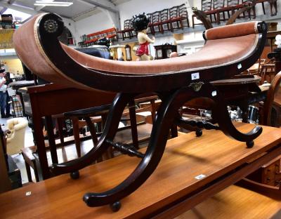 A stained pine window seat of shaped form raised on stretchered outswept supports decorated with simple brass roundels, 58 x 102 x 36cm.