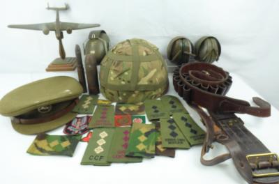Various military collectibles to include an army camouflage hard hat, green ear defenders, a bronze sculpture of a plane, raised on aerial bomb column, gun belt, various cloth badges to include 'SAS' examples, shoulder straps for 'Queen's Lancashire', 'CCF', etc, an officer's Army cap, an artilleries projectile and a spent cartridge with bullet.