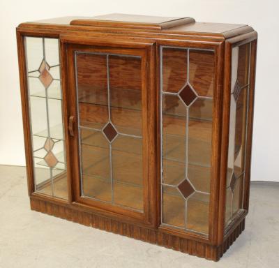 A c1950s oak Art Deco style display cabinet, stepped top over one central stained glass door with glass panels to front and sides, to a plinth base, two interior glass shelves, 117 x 114cm.