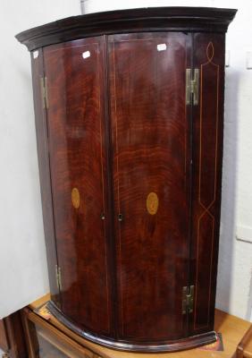 A George III mahogany two-door bow-front corner cabinet, the doors with floral paterae inlay, three internal shelves and three lower spice drawers, height 62.5cm.