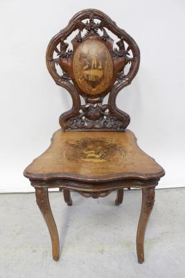 A 19th century Tyrolean hall chair with bas relief carved naturalistic back splat with marquetry central reserve depicting a goatherd in Austrian attire, the serpentine-shaped seat with marquetry and poker work mountain goats, all supported on carved cabriole legs with edelweiss, height 92cm.